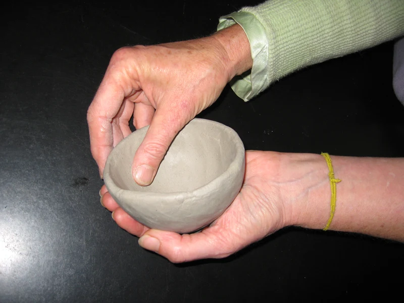 Hands smoothing the surface of a small clay vessel with a stone.